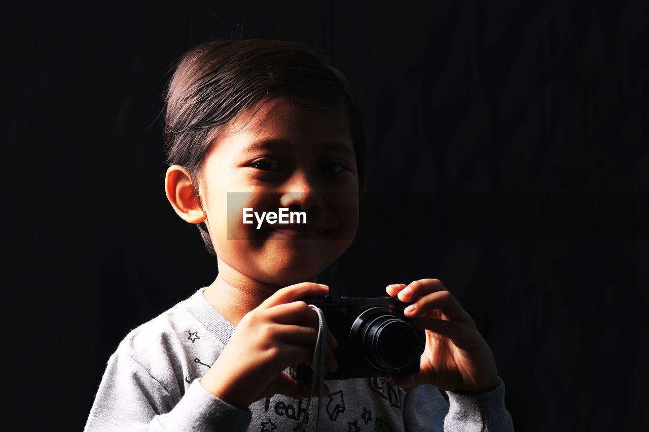 Portrait of boy photographing against black background