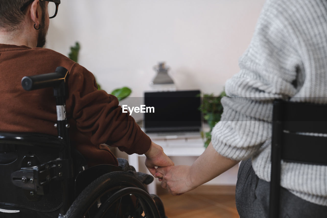 Man in wheelchair holding girlfriend's hand at home