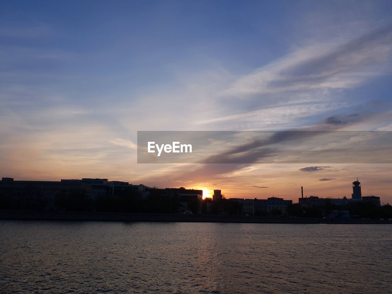 Silhouette buildings by sea against sky during sunset