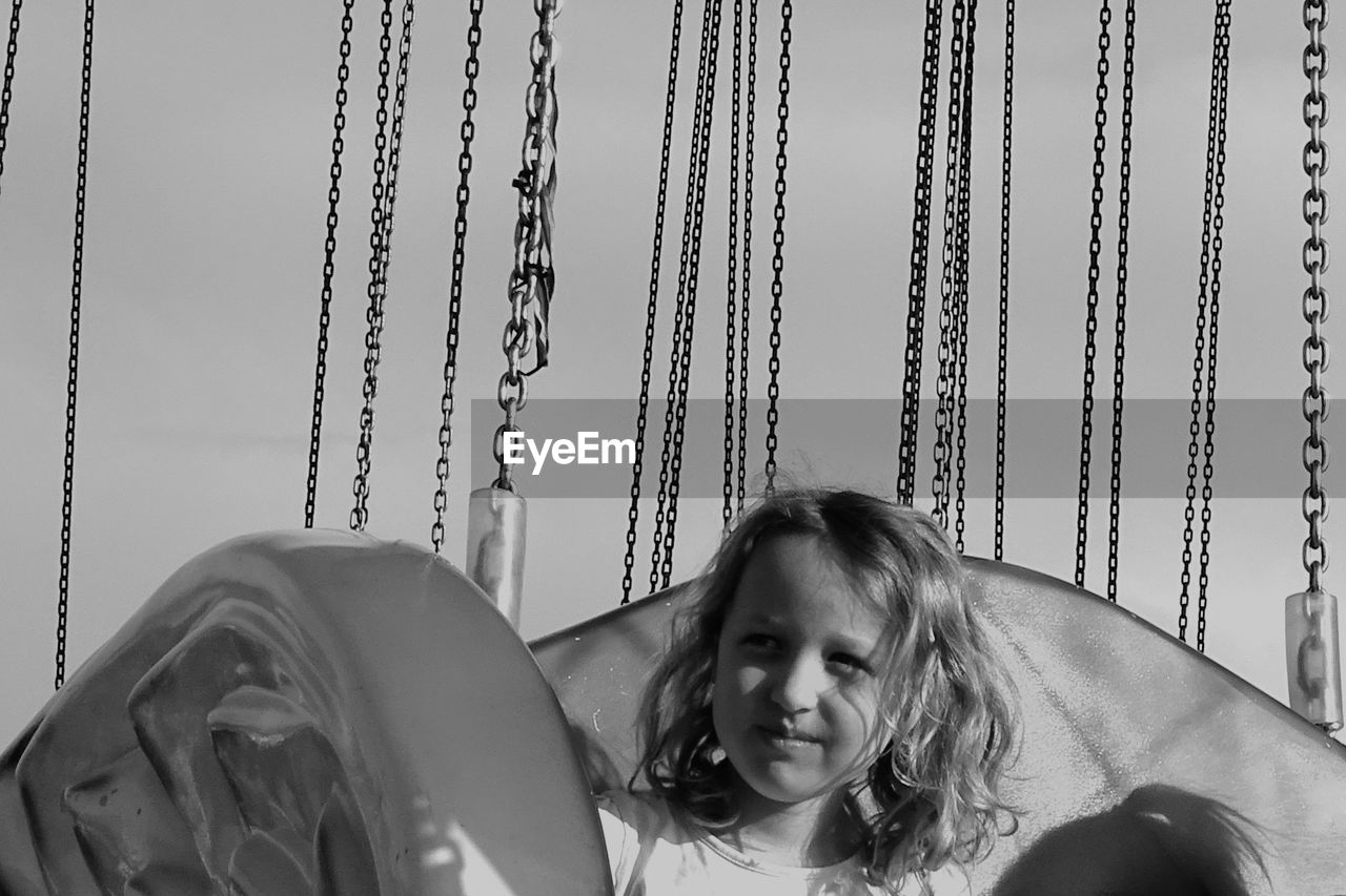 Cute girl looking away while sitting in carousel against sky
