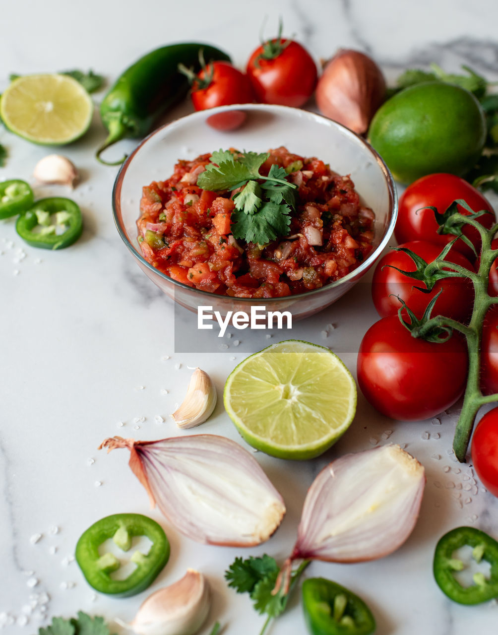 Bowl of fresh salsa with the ingredients on white marble counter.