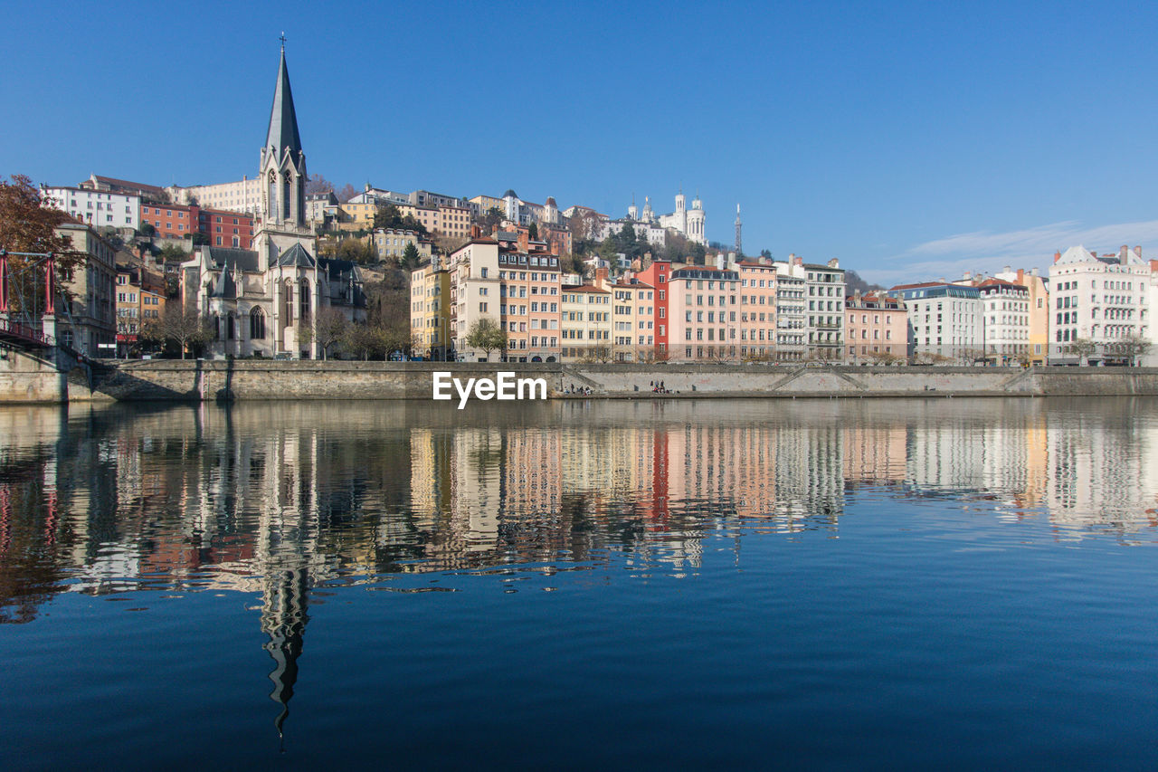 Reflection of buildings in river against clear blue sky