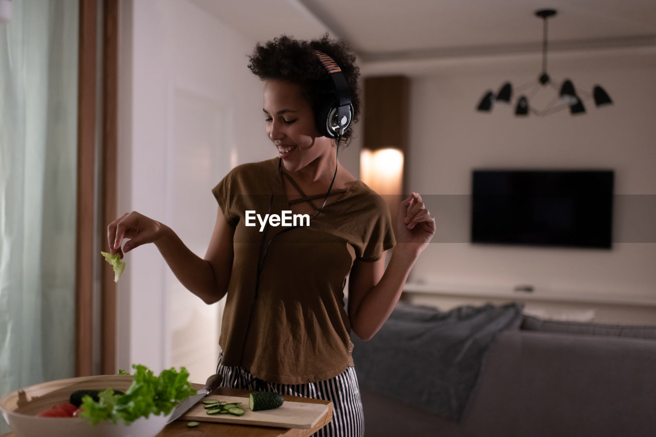 Delighted african american woman in headphones cooking salad