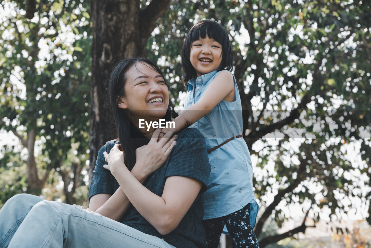 PORTRAIT OF HAPPY WOMAN SITTING ON TREE