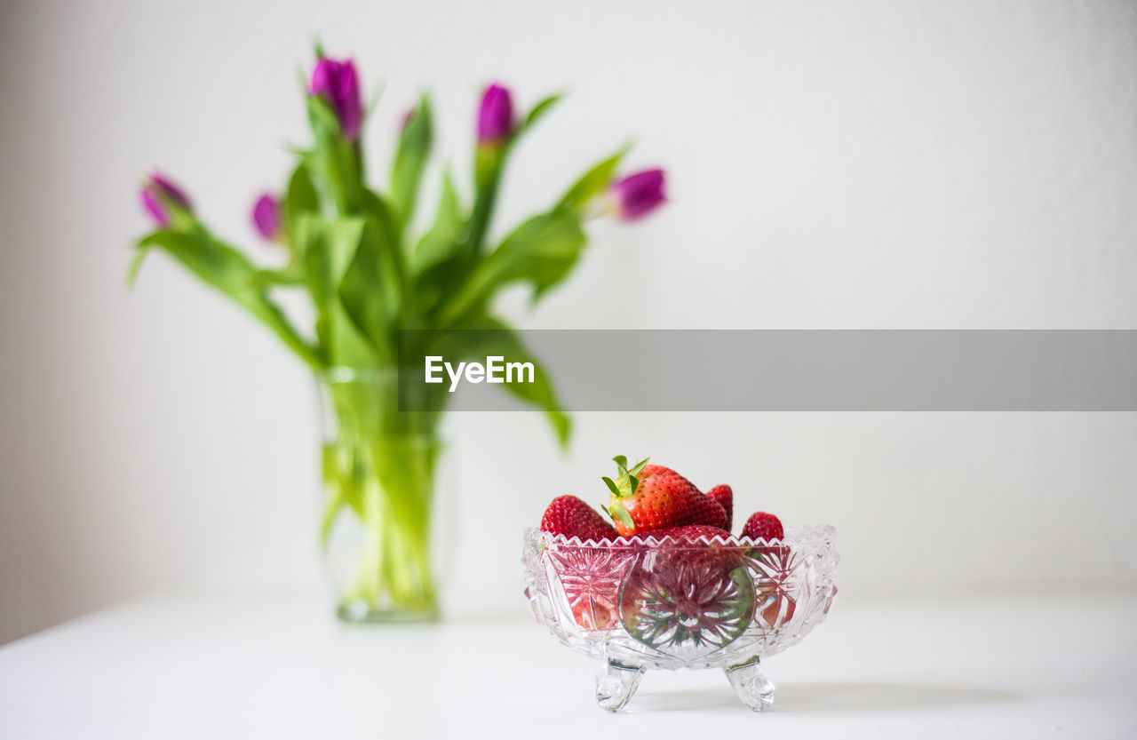 Strawberries in bowl by flower vase on table at home