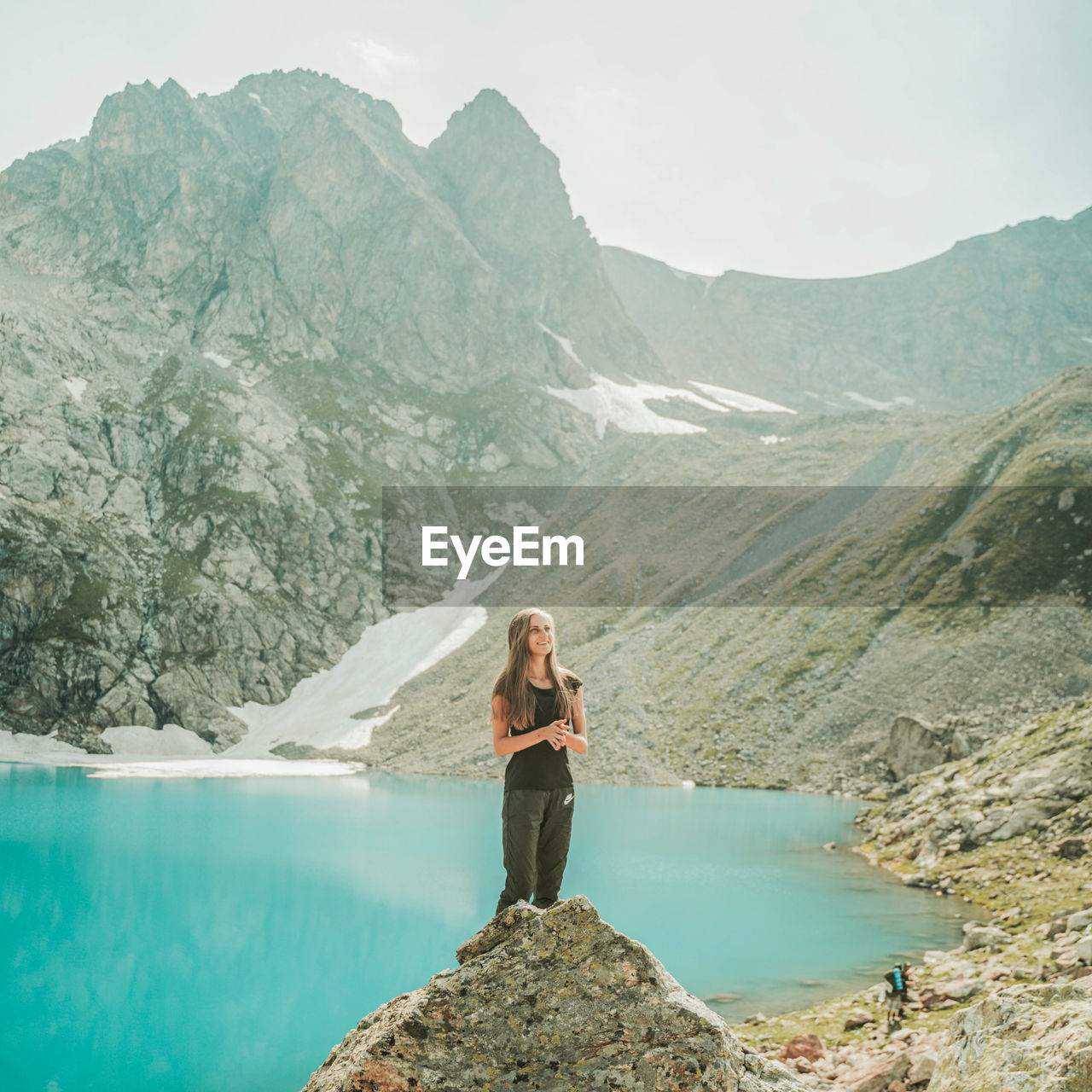 WOMAN STANDING ON ROCKS BY MOUNTAINS