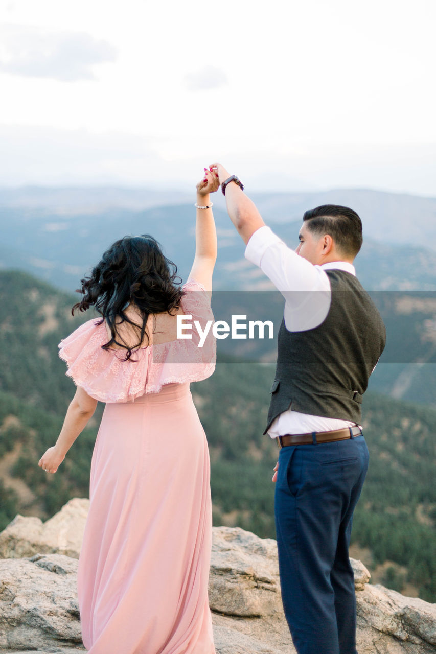 REAR VIEW OF FRIENDS STANDING ON MOUNTAIN