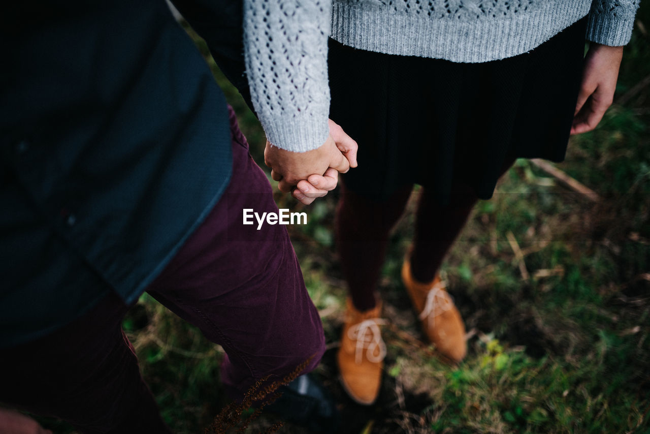 Low section of couple holding hands on field