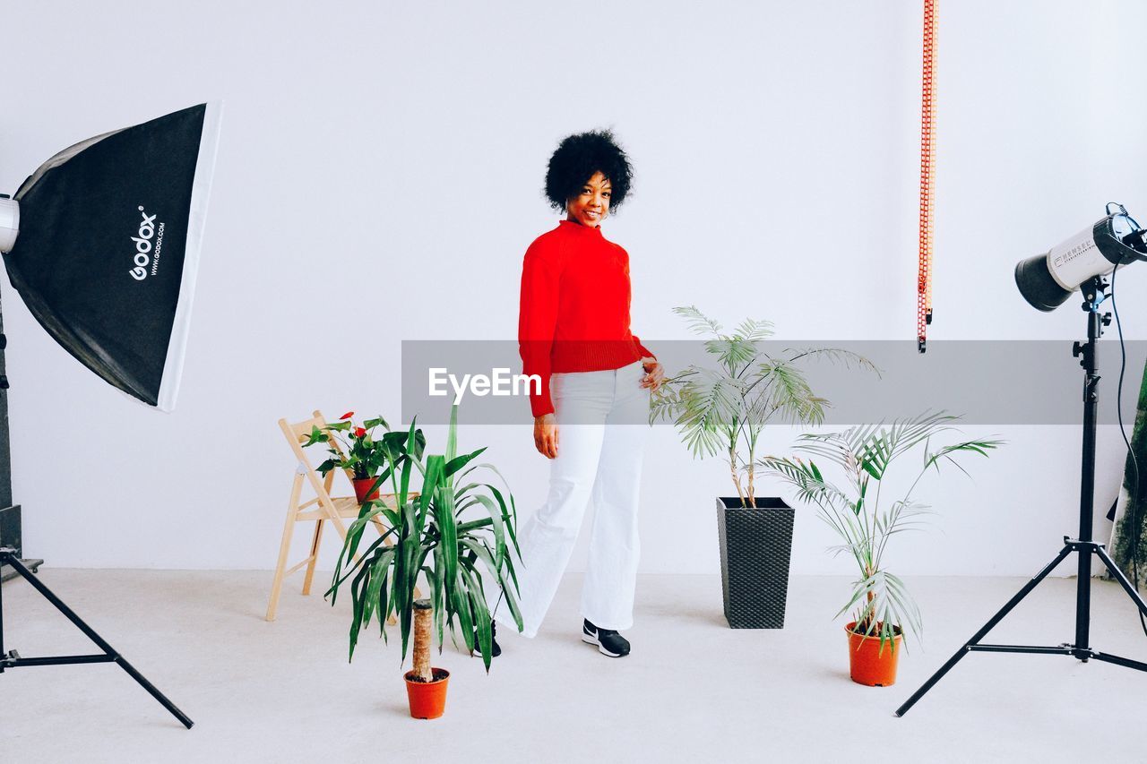 WOMAN STANDING BY POTTED PLANT ON WALL