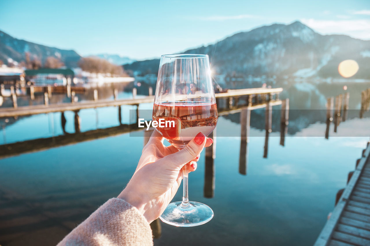 Female hand with glass of rose wine. cozy pier on the coast of lake tegernsee. mountains in bavaria