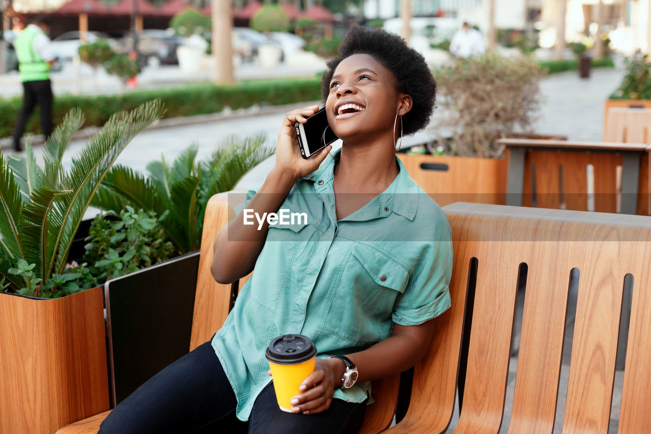 Cheerful young woman talking over smart phone while sitting at cafe