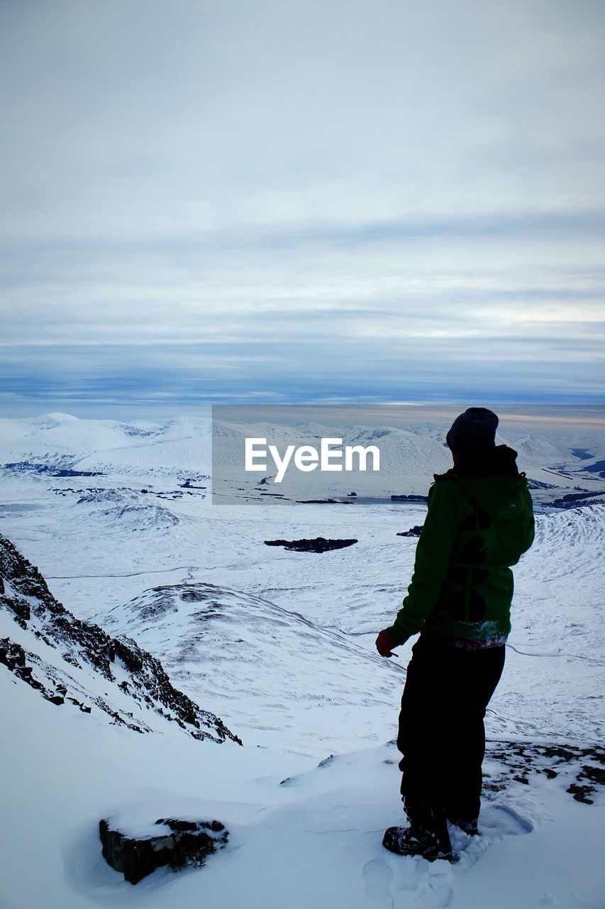 Full length of man standing on snowcapped mountain against cloudy sky
