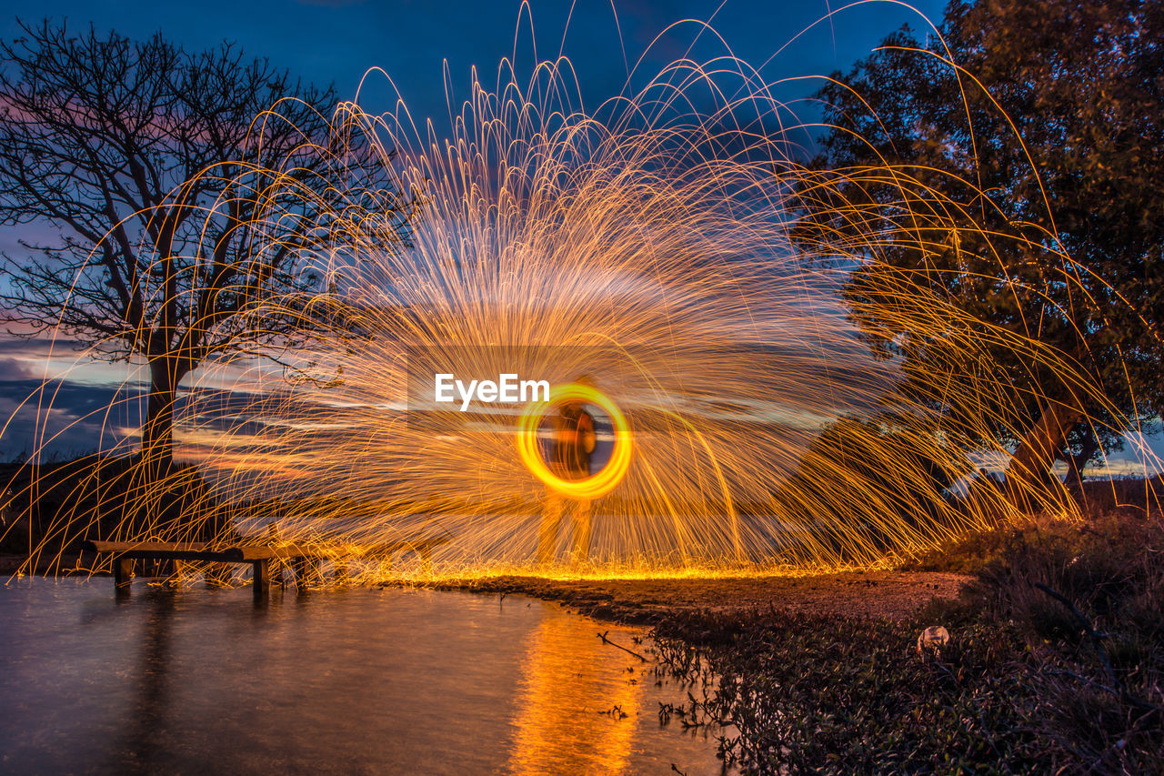 Man spinning wire wool by river at dusk