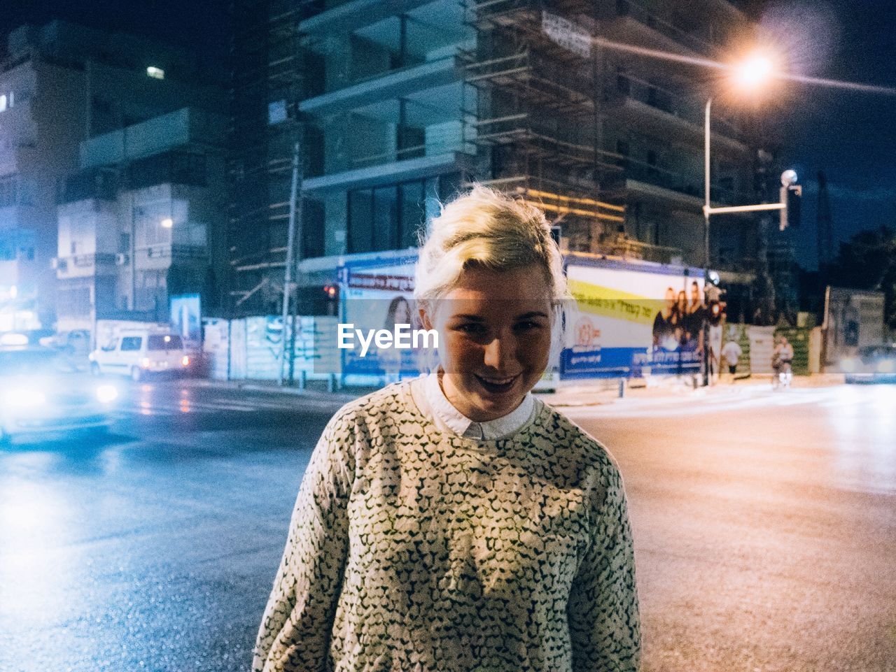 Portrait of smiling woman standing on illuminated street