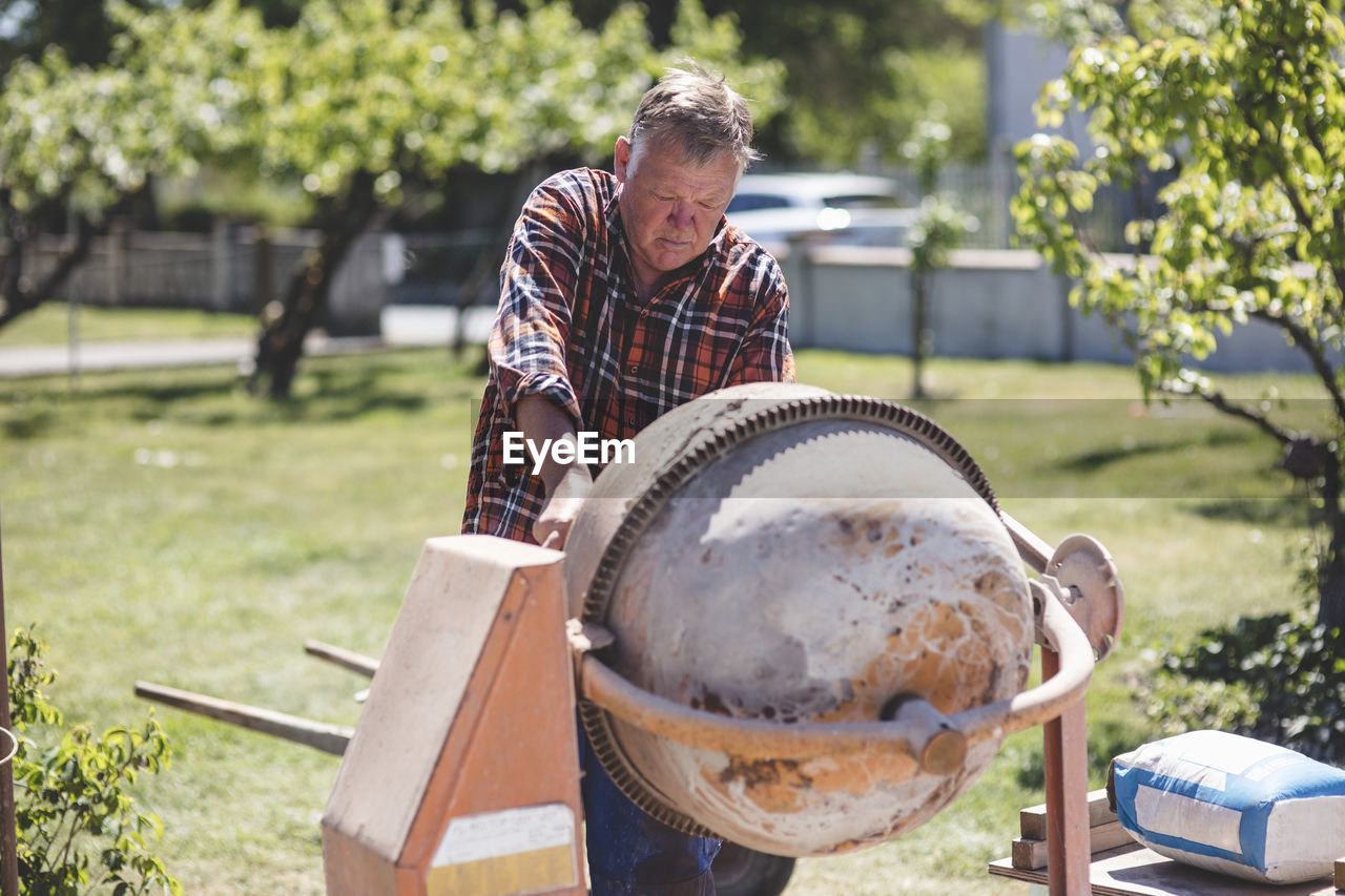 Senior man using cement mixer at yard