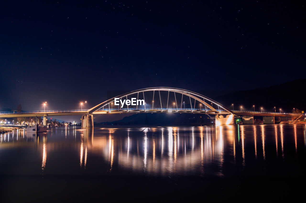 Illuminated bridge over river against sky at night