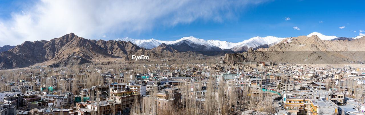 panoramic view of townscape by mountains against sky
