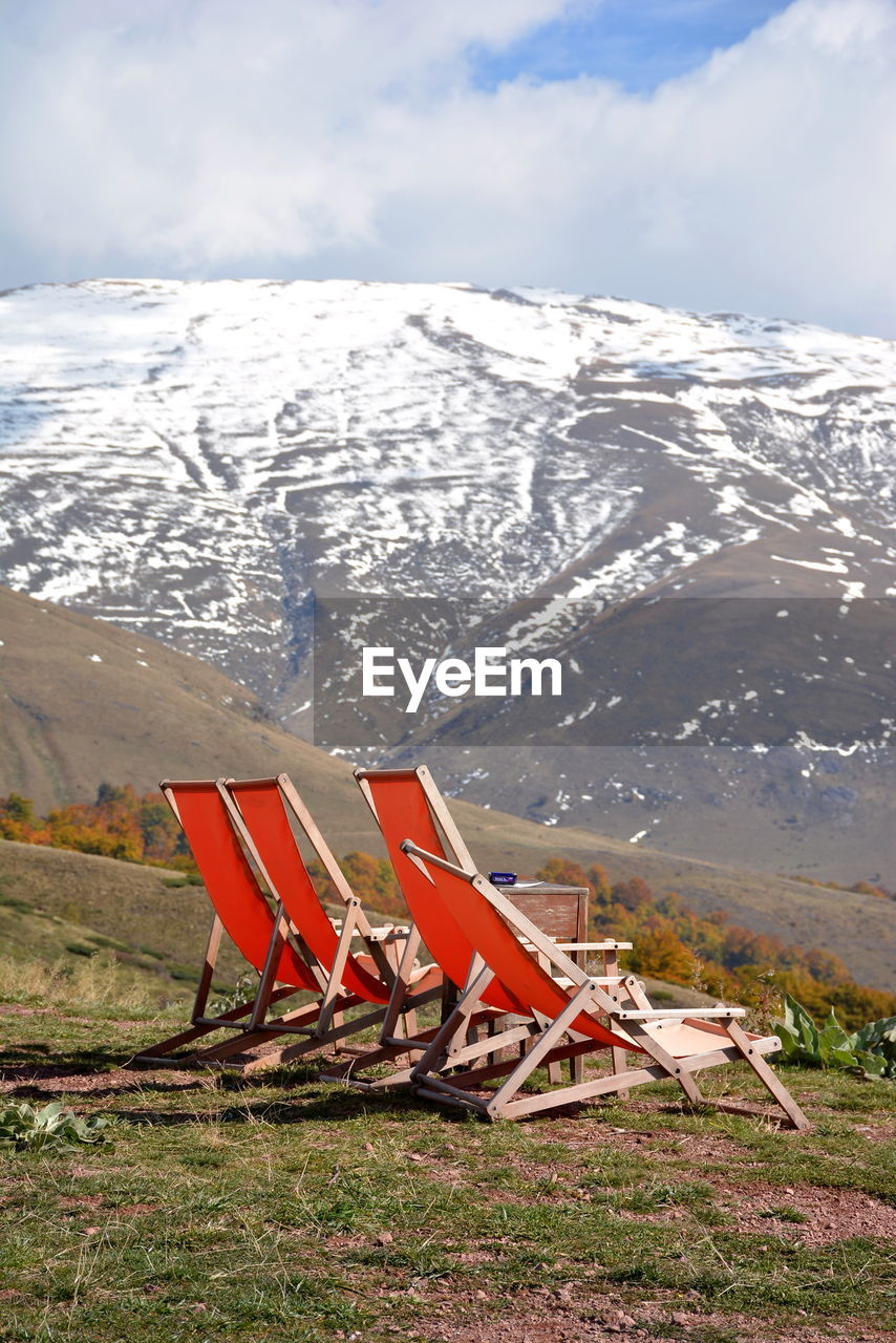 Empty red deck chairs against snowcapped mountains