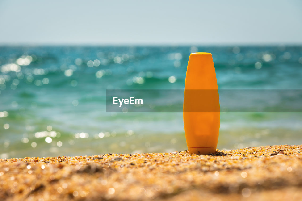 Empty cosmetic skin care cream or sunscreen on sandy beach on sea background. a yellow bottle of