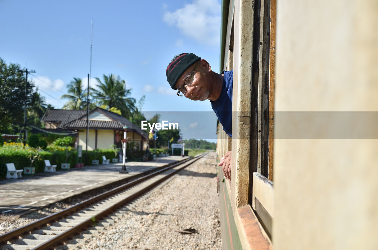 Portrait of man peeking out from train against sky