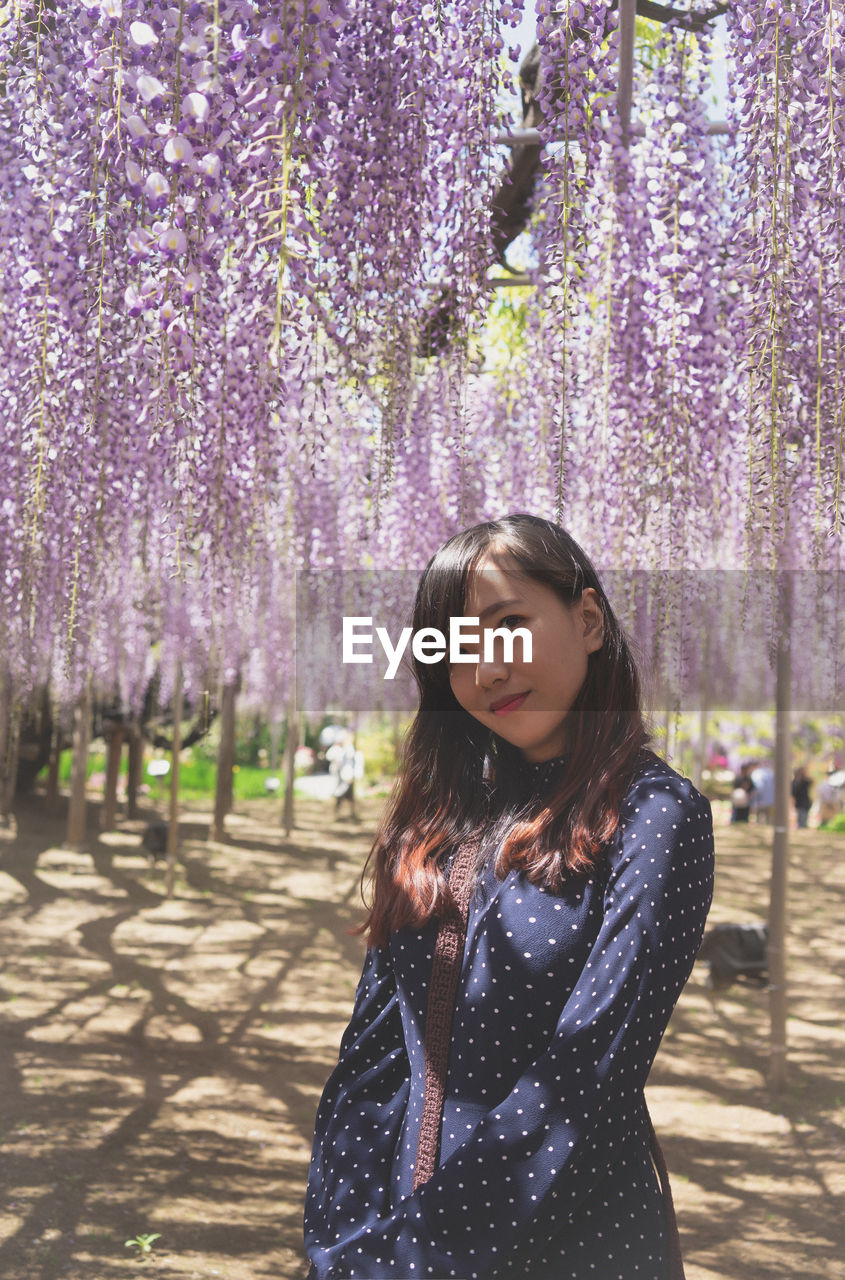 Beautiful young woman standing against pink flower at park