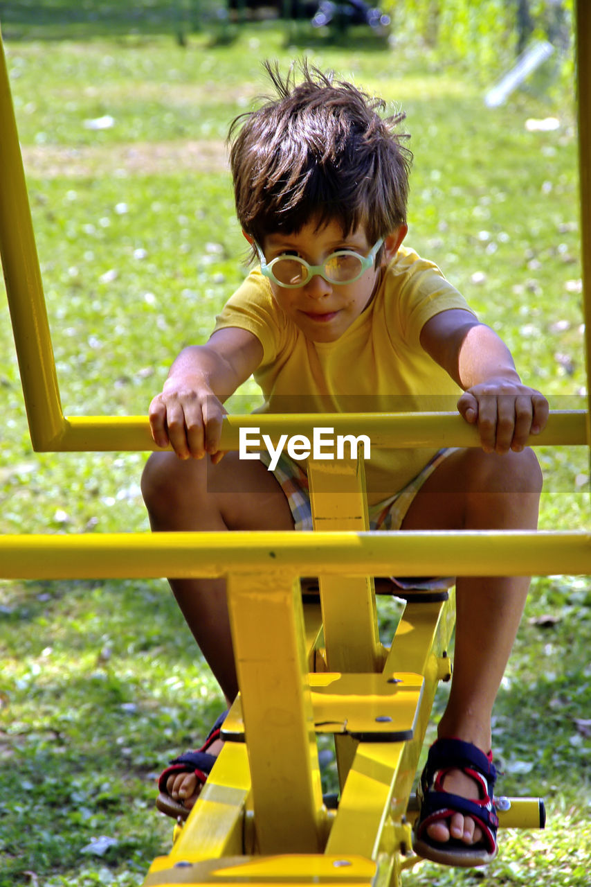 REAR VIEW OF BOY SITTING ON YELLOW PLAYING