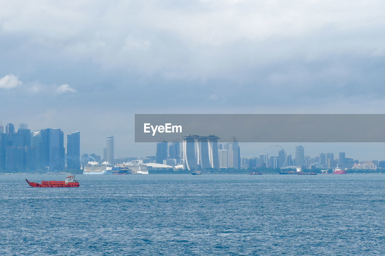 Sailboats in sea by buildings against sky