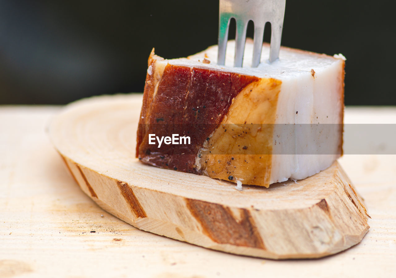 Piece of lard or bacon skewered with a fork on a wooden cutting board, close up