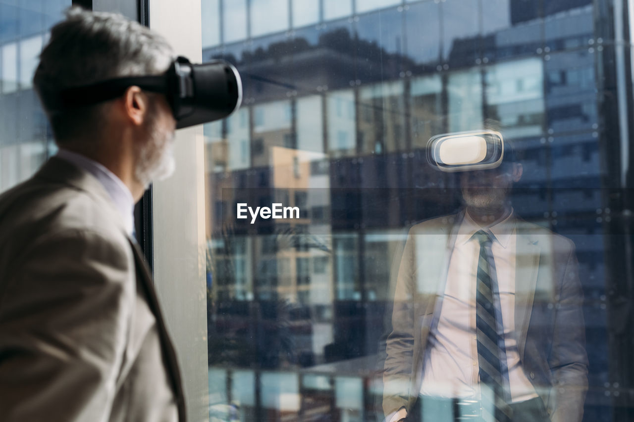 Mature businessman wearing virtual reality simulator standing in front of window