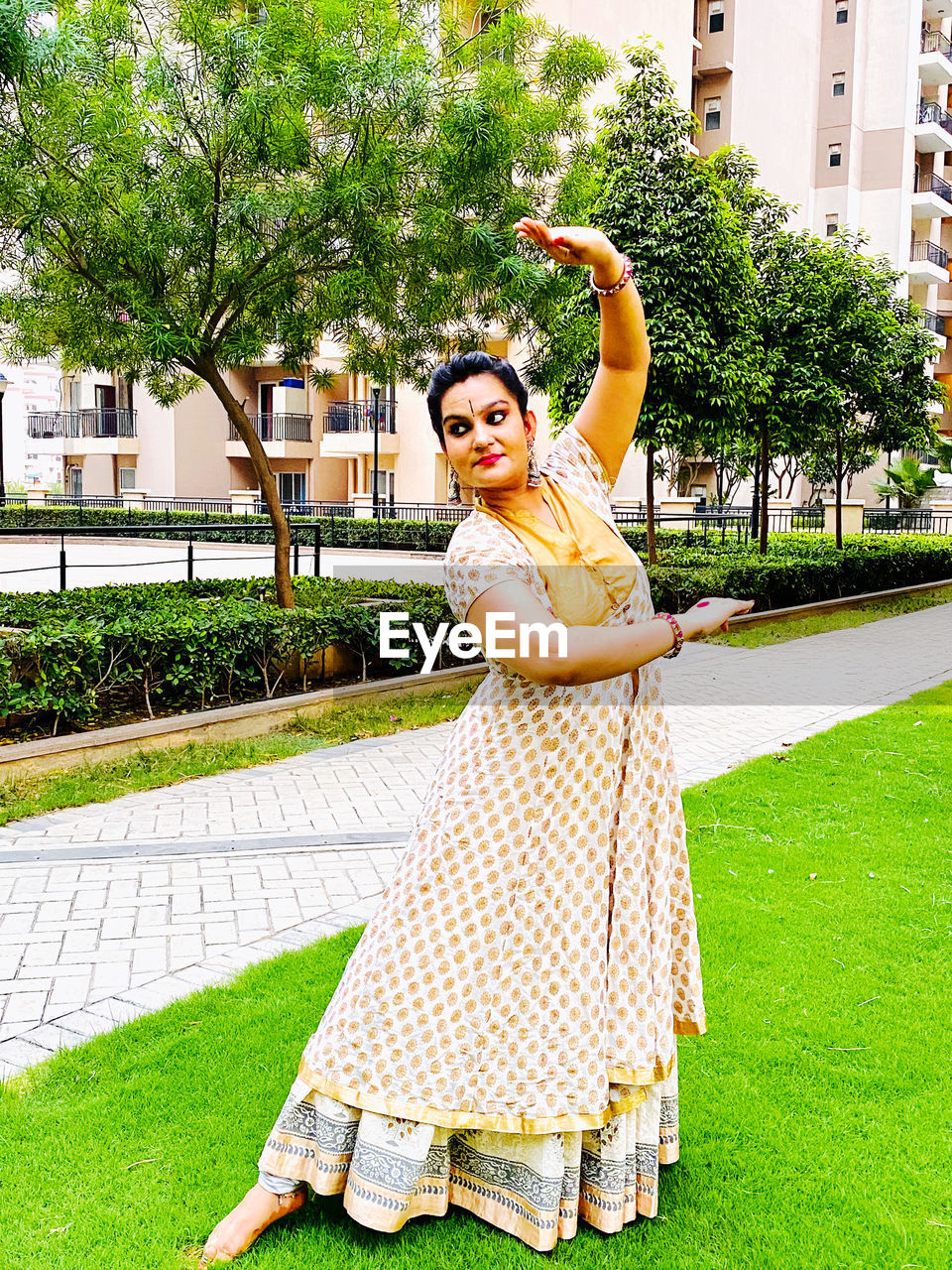 Portrait of smiling woman standing by plants, making a kathak pose