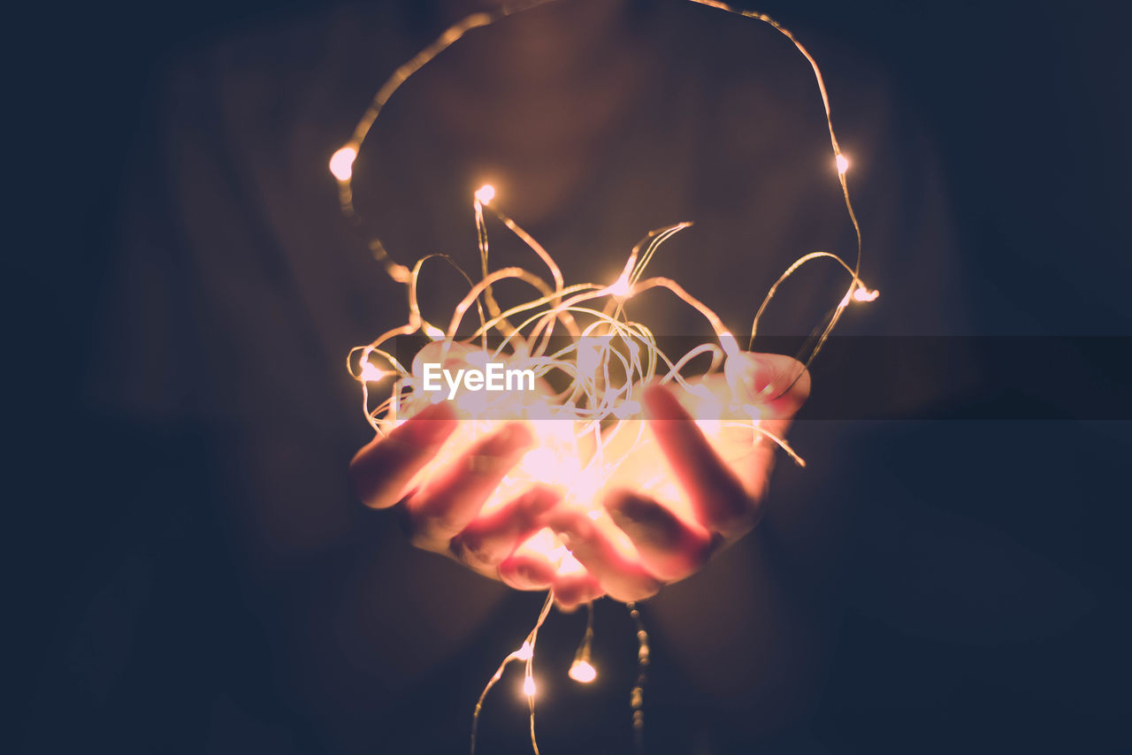 Midsection of person holding illuminated string lights in dark