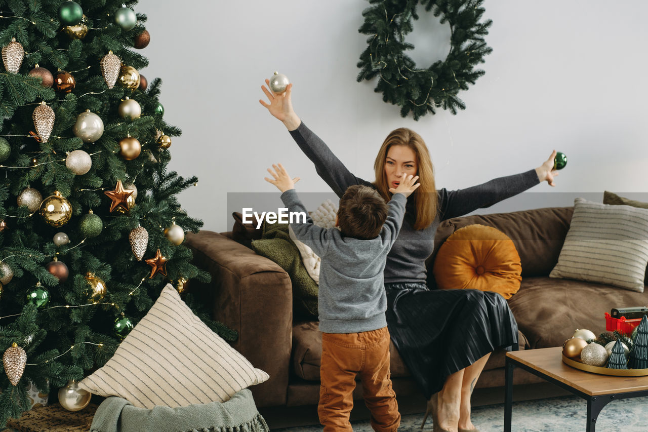 Mother with child playing near christmas tree. child unpacking gifts, woman enjoy christmas tree