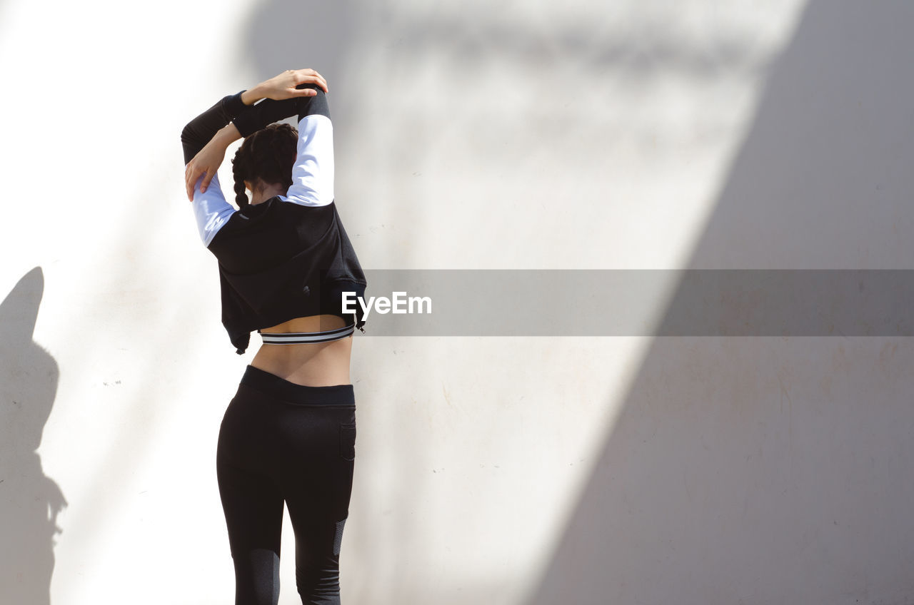Rear view of woman stretching against white wall