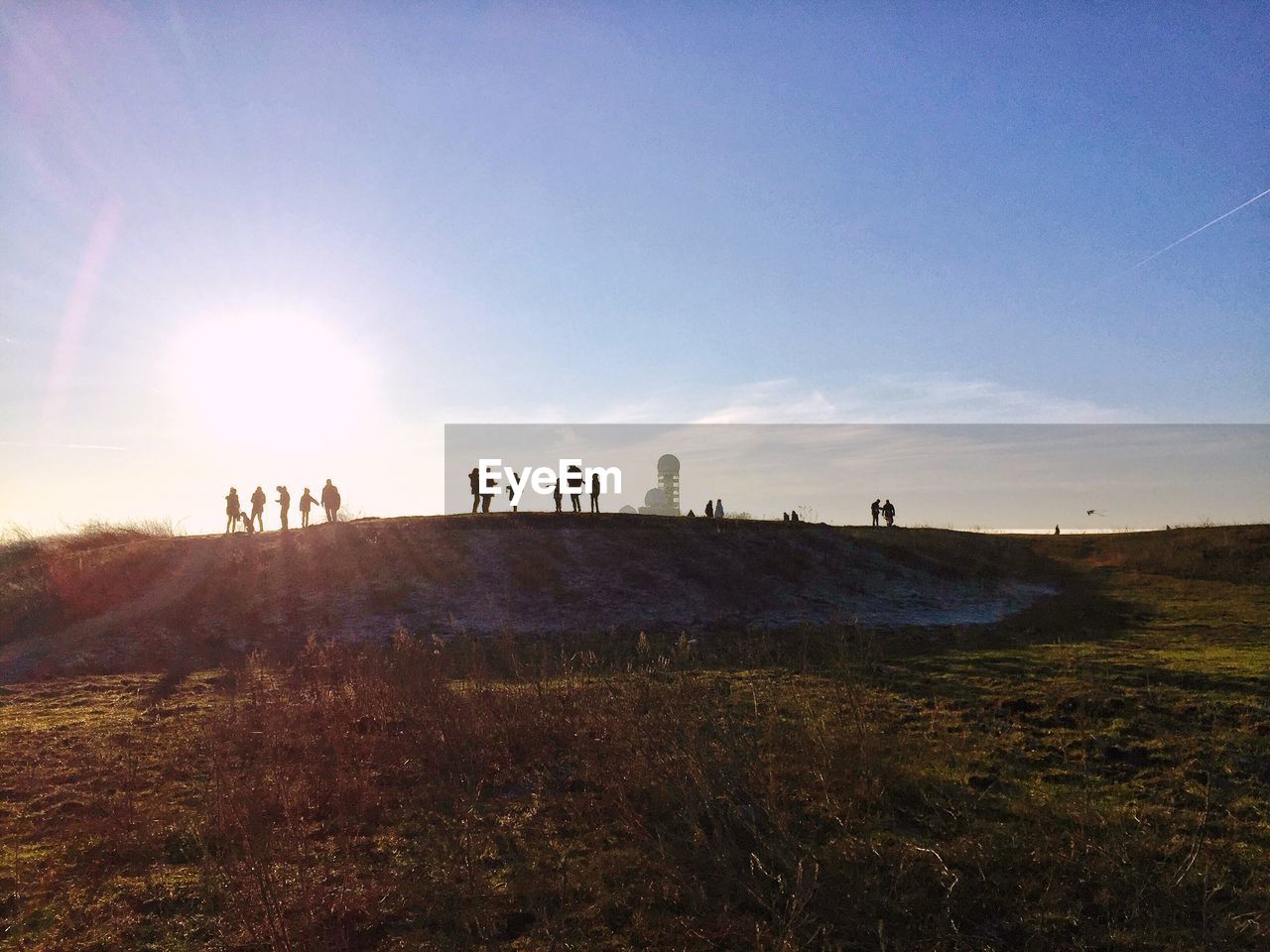 People by field on hill against sky