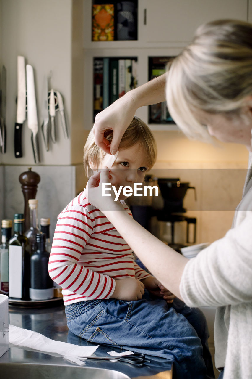 Mother applying bandage on daughter's face in kitchen at home