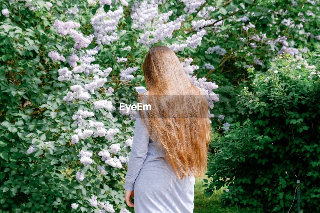 REAR VIEW OF WOMAN STANDING ON FLOWERING PLANTS