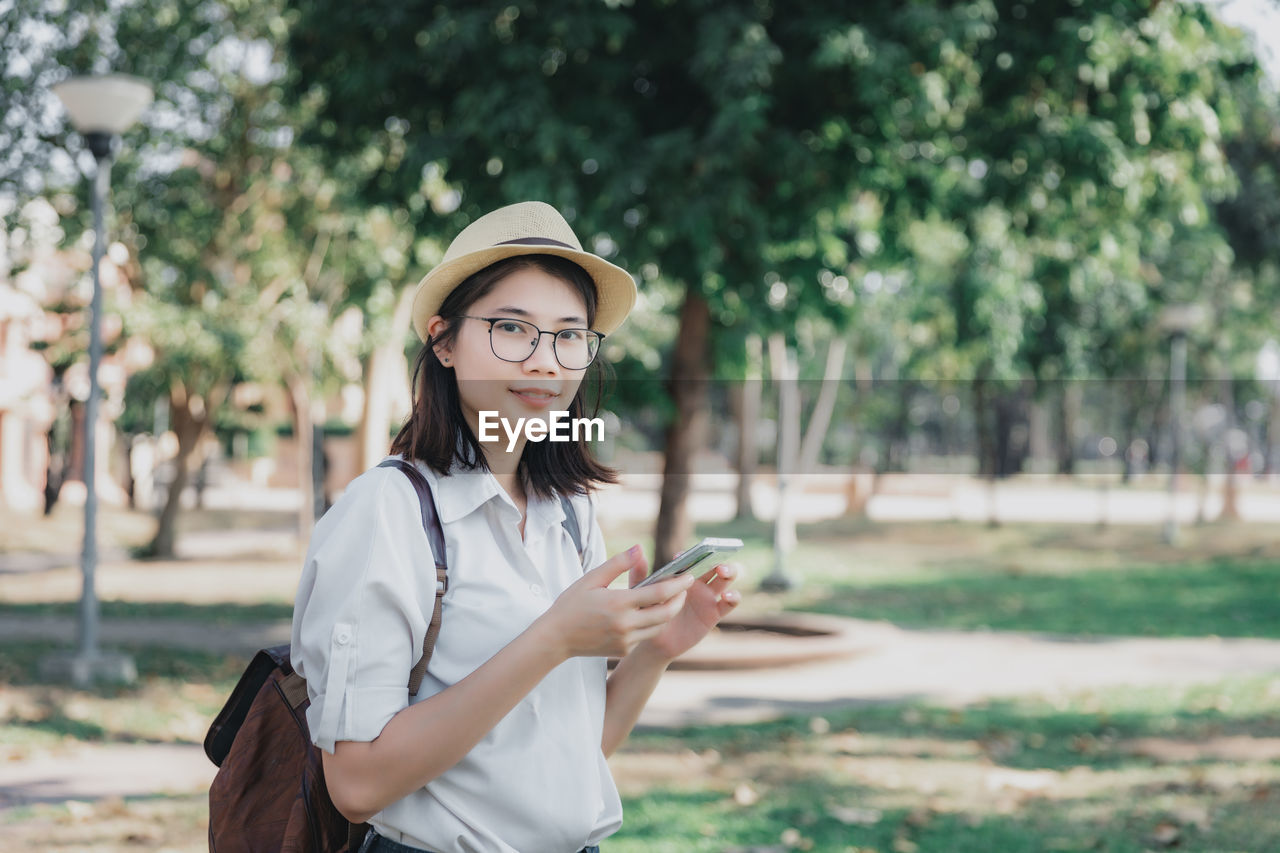 Young asian woman with backpack and straw hat using mobile phone