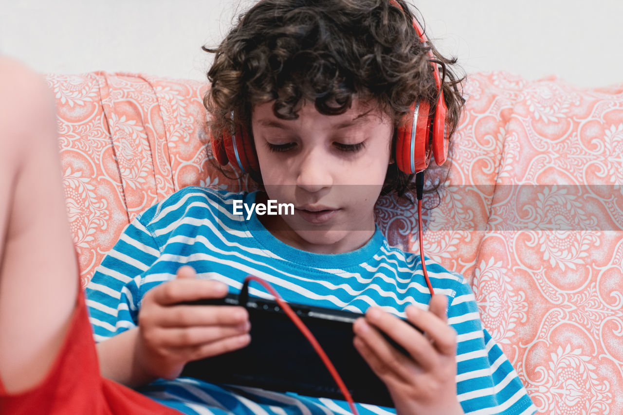 Boy using mobile phone while wearing headphones at home