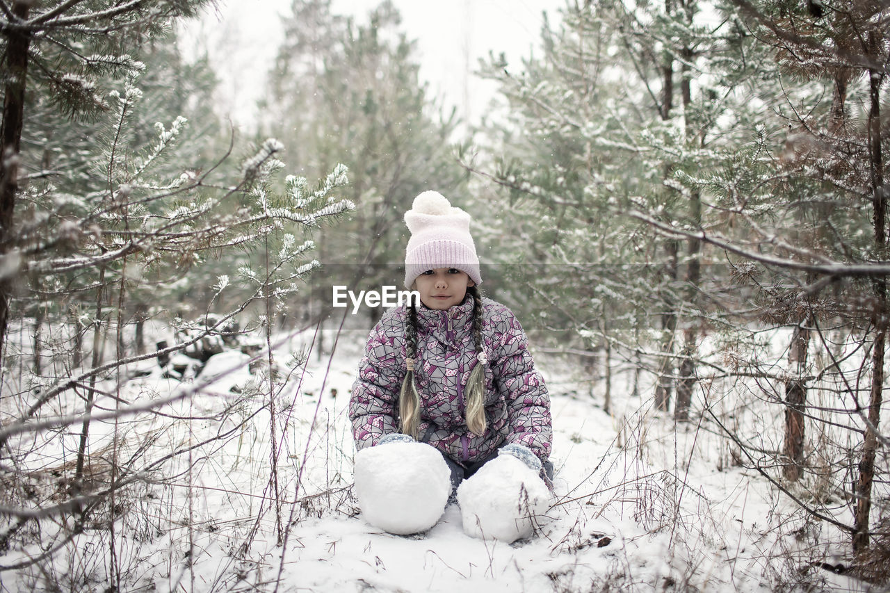 GIRL SITTING ON SNOW COVERED LAND DURING WINTER