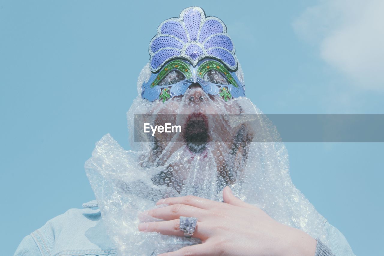 Low angle view of woman wearing mask and bubble wrap standing against sky