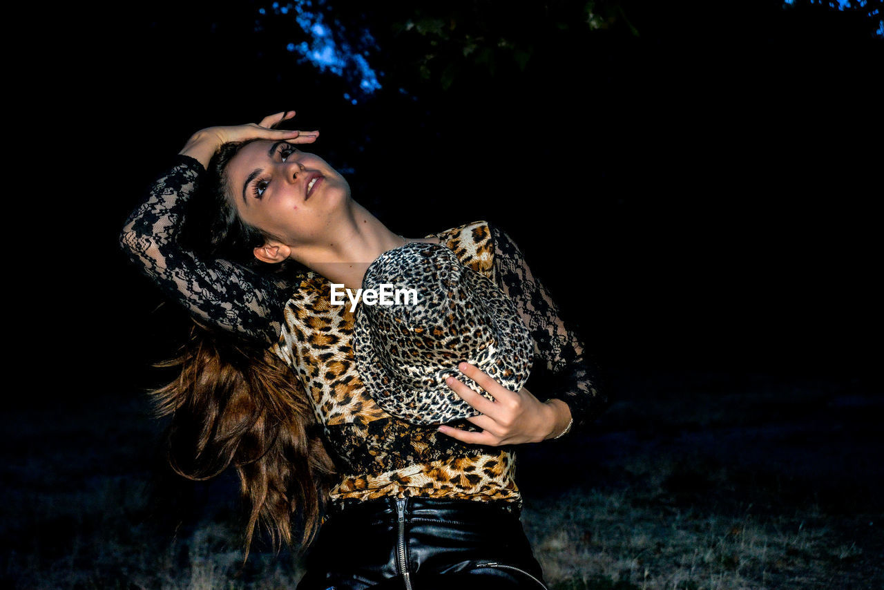 BEAUTIFUL YOUNG WOMAN LOOKING AWAY AGAINST BLACK BACKGROUND