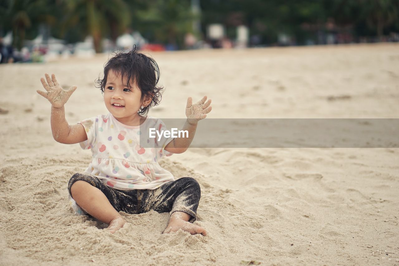 Thoughtful baby girl playing with sand while sitting at beach
