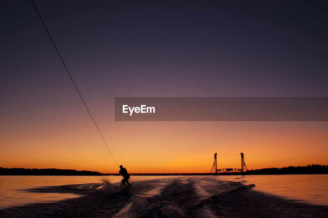 Silhouette man wakesurfing during sunset