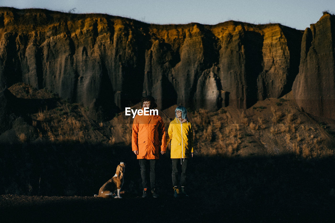 Full length of couple with dog standing against rock mountains