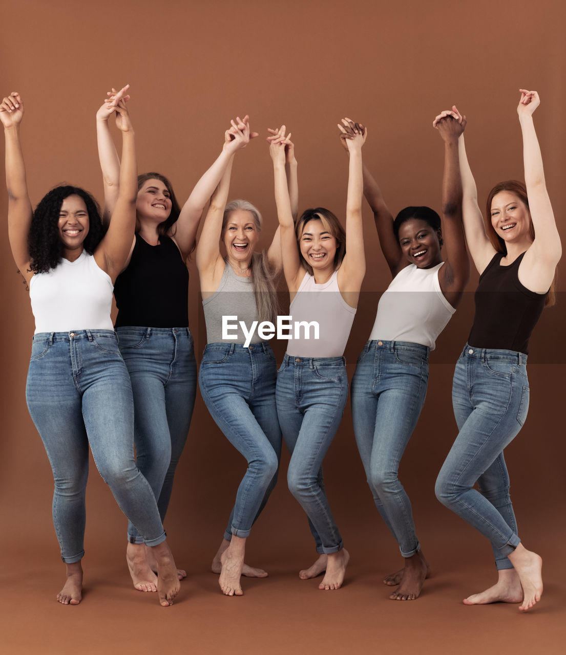 Six happy women raised their hands up together over brown background	