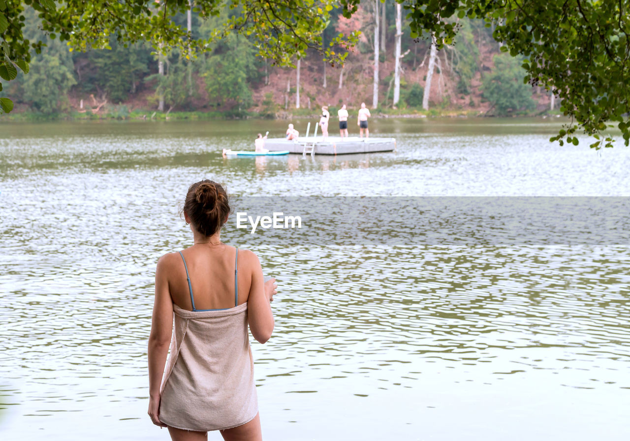 water, rear view, one person, tree, nature, plant, lake, adult, leisure activity, lifestyles, beauty in nature, vacation, trip, holiday, day, tranquility, women, three quarter length, relaxation, outdoors, summer, young adult, travel, tranquil scene, standing, back, clothing, casual clothing, idyllic, land, scenics - nature, hairstyle, men