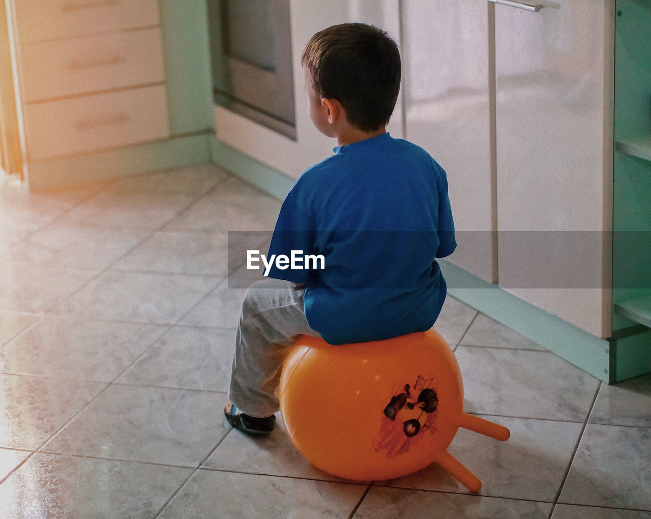Rear view of boy sitting on balloon at home