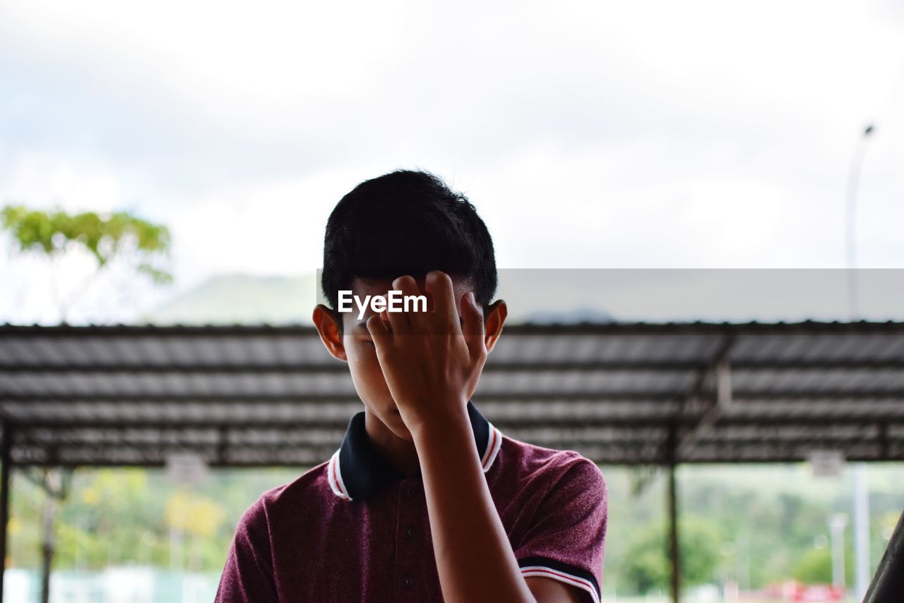 Close-up of man hiding face against sky