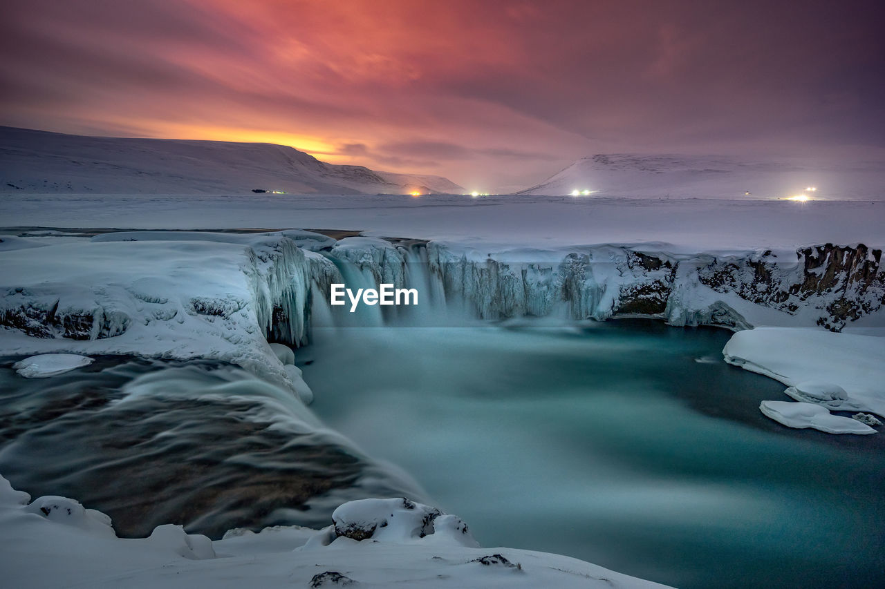 Scenic view godafoss falls on snowcapped mountains against sky during sunset