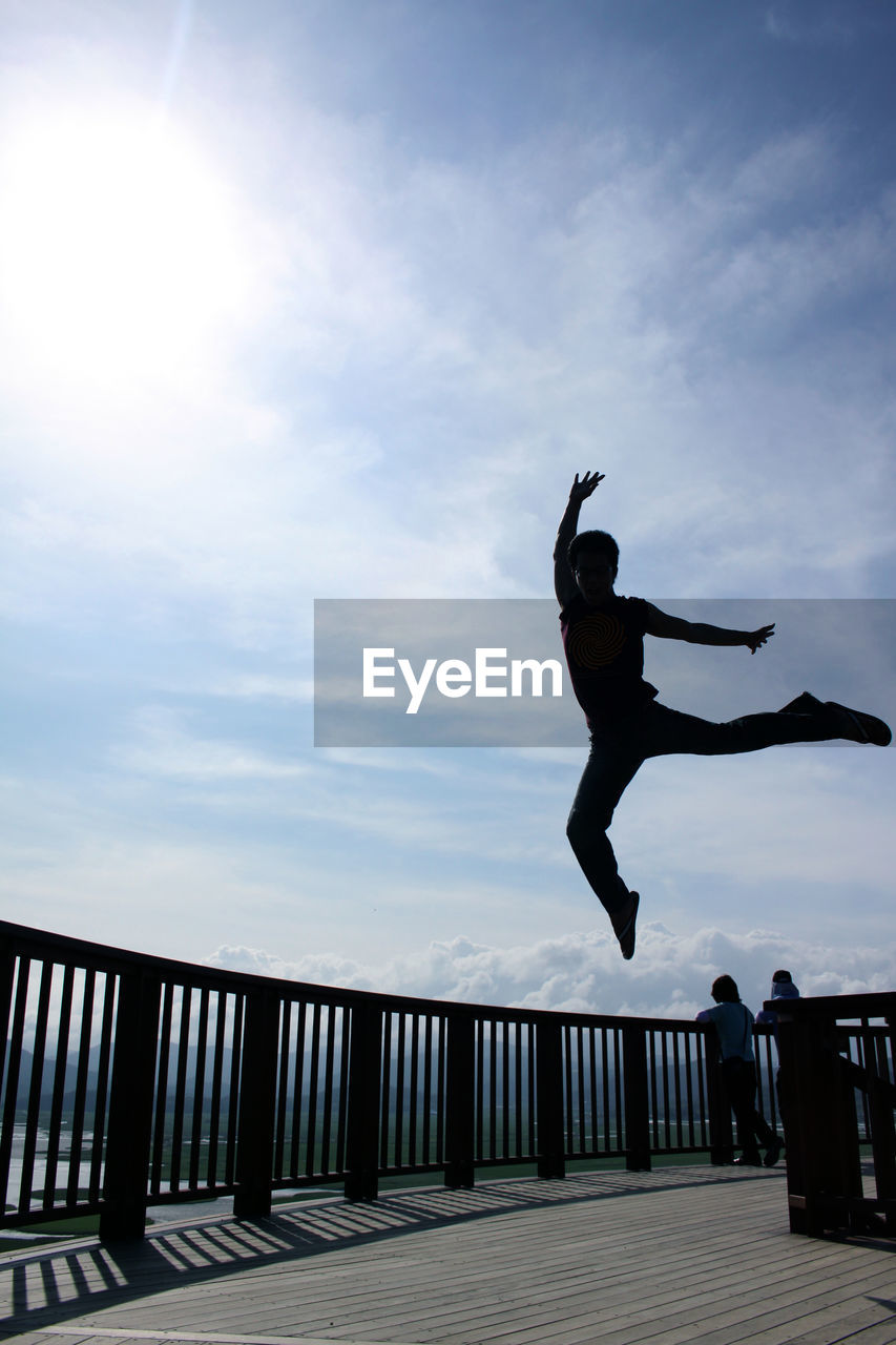 LOW ANGLE VIEW OF MAN JUMPING AGAINST BUILT STRUCTURE